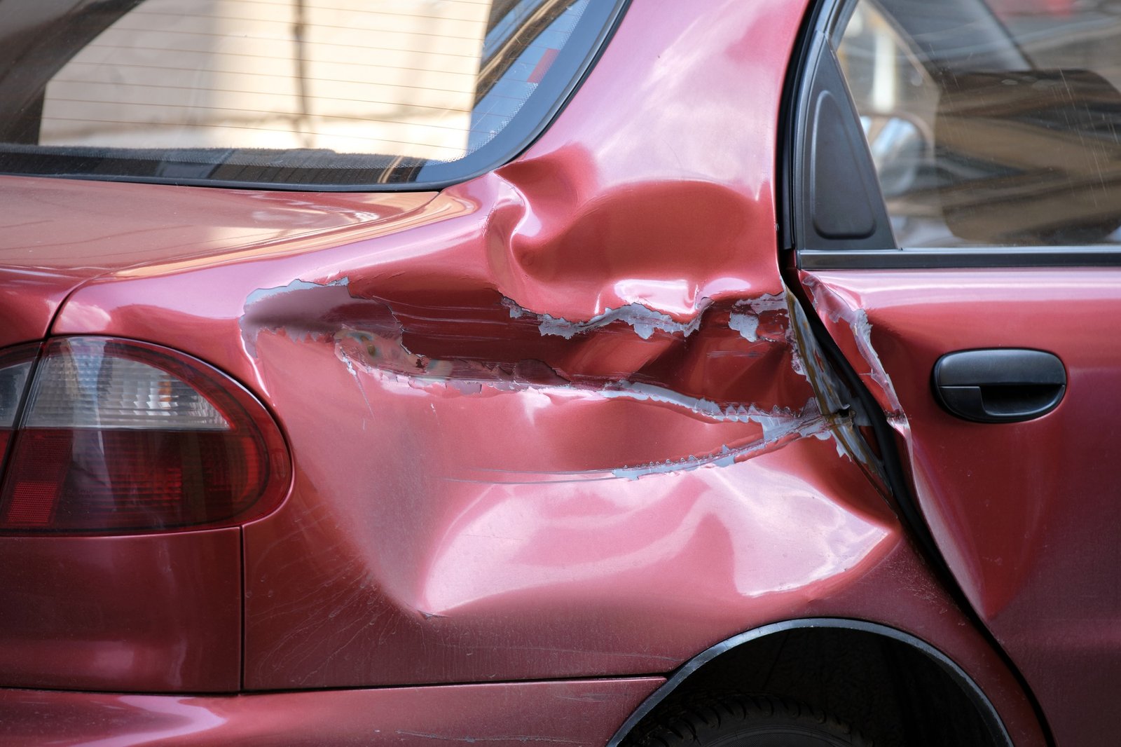 Dented car with damaged body parked on city street side.