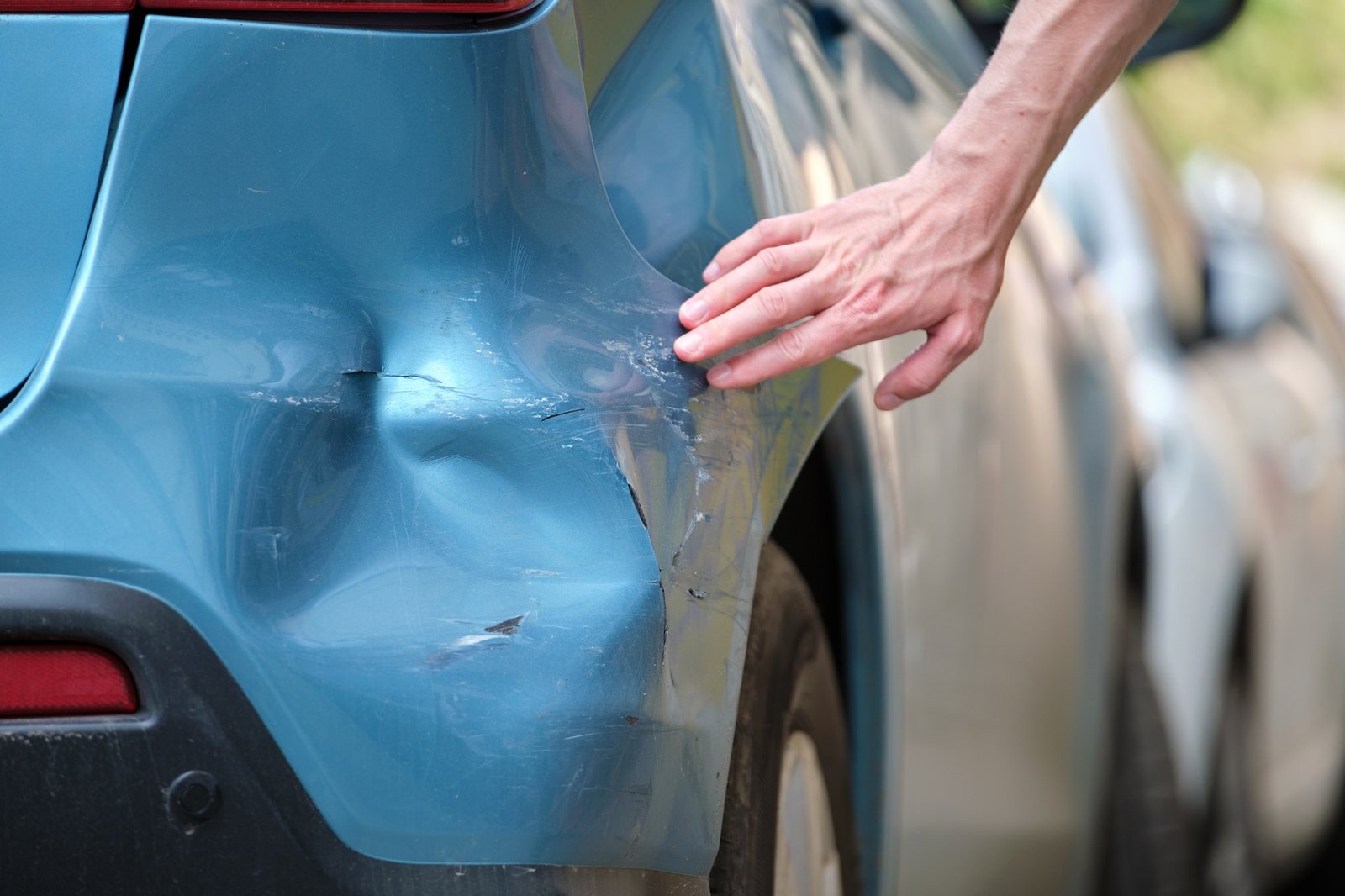 Driver hand examining dented car with damaged fender